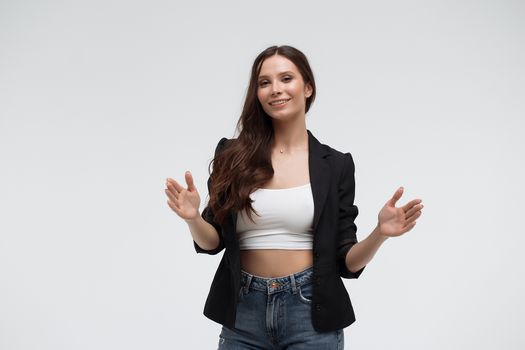 Positive optimistic young female in casual clothes gesturing and showing big size with hands while standing against white background