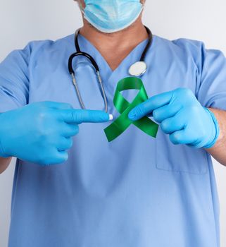 doctor in blue uniform and latex gloves holds a green ribbon as a symbol of early research and disease control, symbol of Lyme disease, kidney transplantation and organ donation