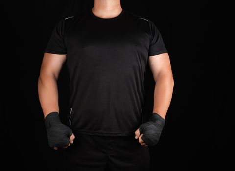 adult athlete in black uniform is standing in a rack with strained muscles, his hands are wrapped in a black textile bandage, dark background