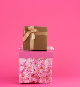 closed pink and golden cardboard boxes with a bow on a pink background, close up