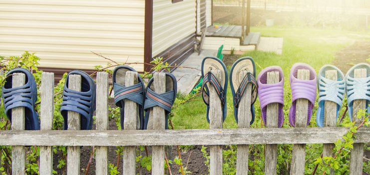 Summer shoes flip flops for a happy friendly family hang on a wooden fence outdoors on a Sunny summer day.