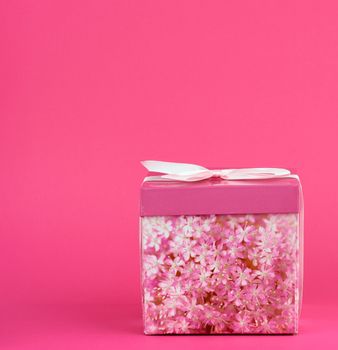 closed pink cardboard box with a bow on a pink background, copy space