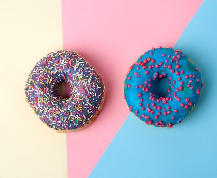 round baked donut with colored sugar sprinkles and with blue sugar glaze on a pink-yellow background, top view