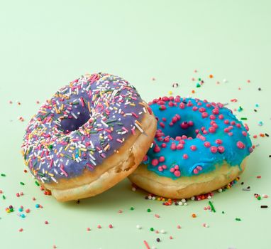 round baked donut with colored sugar sprinkles and with blue sugar icing on a green background, close up