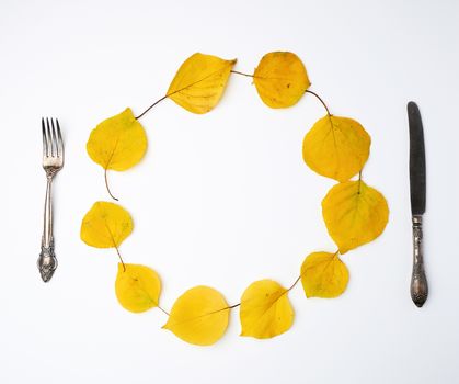 fork, knife and round wreath of yellow dried apricot leaves on a white background, copy space