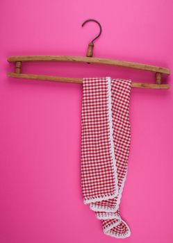 red checkered kitchen towel hanging on a vintage wooden hanger, pink background