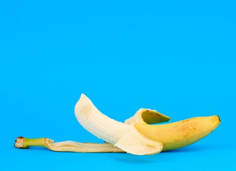peeled ripe yellow banana on a blue background, copy space