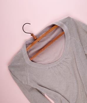 beige female sweater hanging on a vintage wooden hanger, beige background