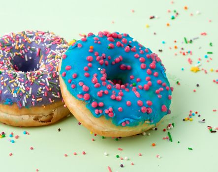 round baked donut with colored sugar sprinkles and with blue sugar icing on a green background, close up