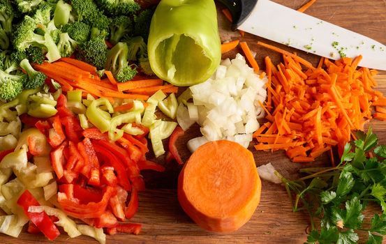 chopped vegetables peppers, broccoli, onions, carrots on a wooden board, top view