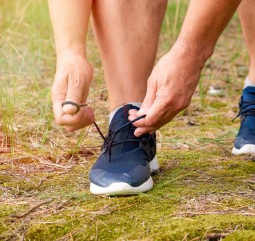 athlete in black uniform crouched and tying the laces on blue sneakers in the middle of the forest, concept of a healthy lifestyle and jogging