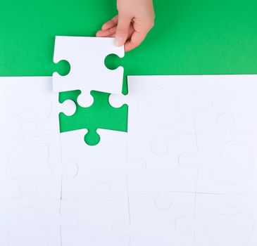 female hand puts empty white big puzzles on a green background, top view