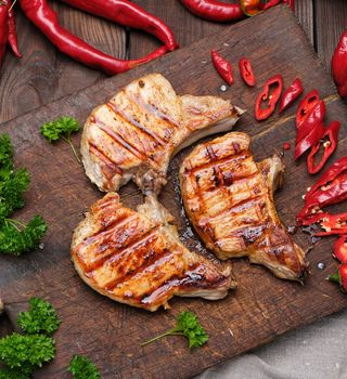 pork fried steak on the rib lies on a vintage brown wooden board, next to fresh red chili peppers, top view