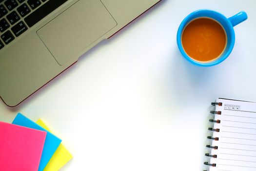 Top view of computer laptop, a cup of coffee and the other office accessories on the white table workplace