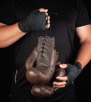 athlete in black clothes holds very old vintage leather brown boxing gloves, low key