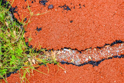 Cracked surface of playground rubber with green grass