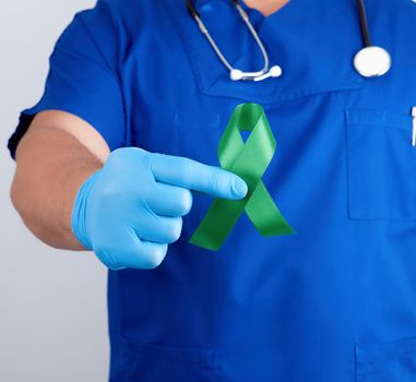 doctor in blue uniform and latex gloves holds a green ribbon as a symbol of early research and disease control, symbol of Lyme disease, kidney transplantation and organ donation