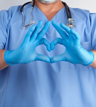 doctor in blue uniform and latex gloves shows a heart gesture near his chest, white background