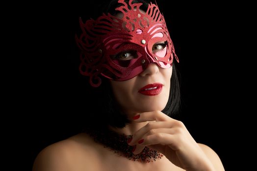 beautiful adult woman of Caucasian appearance with black hair wearing a red shiny carnival mask, lips parted and painted with red lipstick, dark background