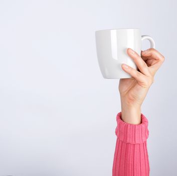 female hand in a pink sweater holds a gray ceramic cup, white background, breakfast concept