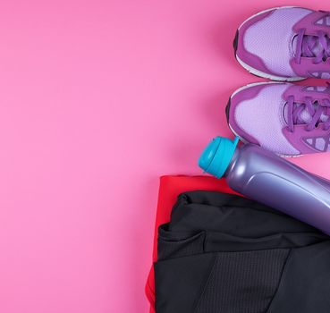 pink women's sneakers, bottle of water, clothes for sports on a pink background, top view, copy space