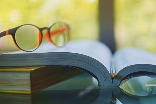 Eyeglasses placed on the opened book with blurred natural background and vintage retro color tone