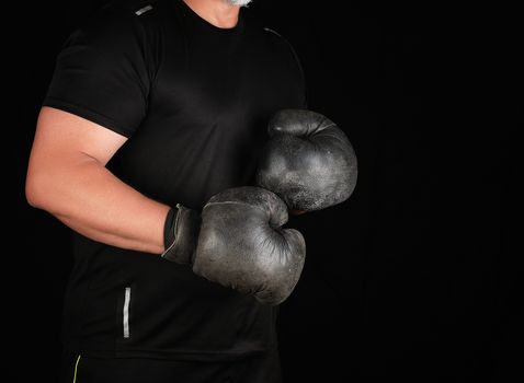 man stands in a boxing rack, wearing very old vintage black boxing gloves on his hands, dark background
