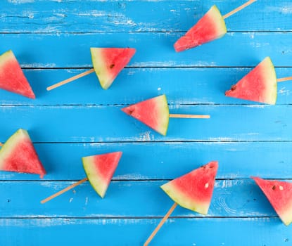 slices of ripe red watermelon on a wooden stick lie randomly on a blue background, flat lay