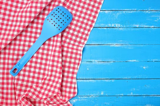 plastic blue spoon with holes on a red textile napkin, wooden background
