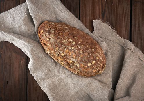 baked oval bread made from rye flour with pumpkin seeds on a gray linen napkin, top view