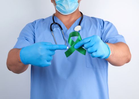 doctor in blue uniform and latex gloves holds a green ribbon as a symbol of early research and disease control, symbol of Lyme disease, kidney transplantation and organ donation