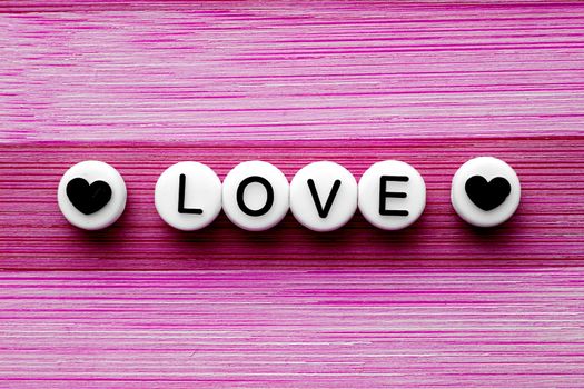 Love text with hearts on the side on a pink wooden table