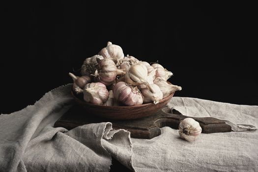 raw unpeeled garlic in a brown ceramic plate on a gray linen napkin, dark background