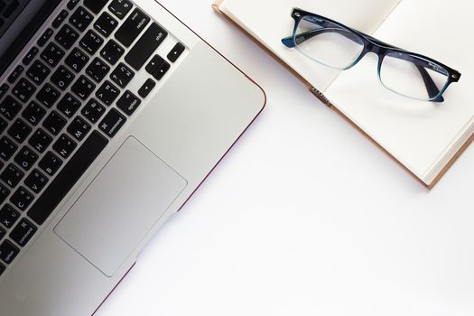 Top view of workspace, computer laptop, notebook and eyeglasses, on the white desk background