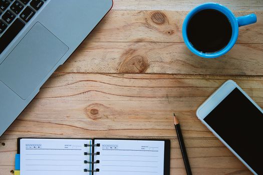 Top view of computer laptop, a cup of coffee, mobile smartphone, notebook and pencil on the wooden table workplace