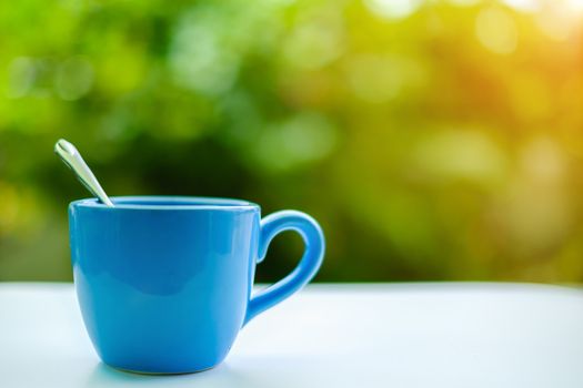 A blue cup of coffee on blurred green natural background