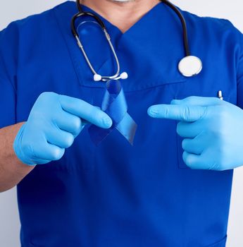 doctor in blue uniform and sterile latex gloves holds a dark blue ribbon, concept of timely research and disease prevention colon malignancies, chronic fatigue syndrome, tuberous sclerosis