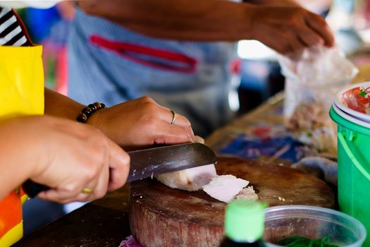 Female street vendor slicing pork for cooking