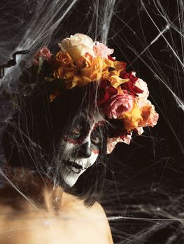 girl with black hair is dressed in a wreath of multi-colored roses and makeup is made on her face Sugar skull to the day of the Dead, close up