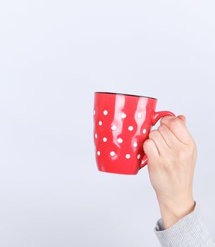 red ceramic cup in a female hand on a white background, hand is raised up