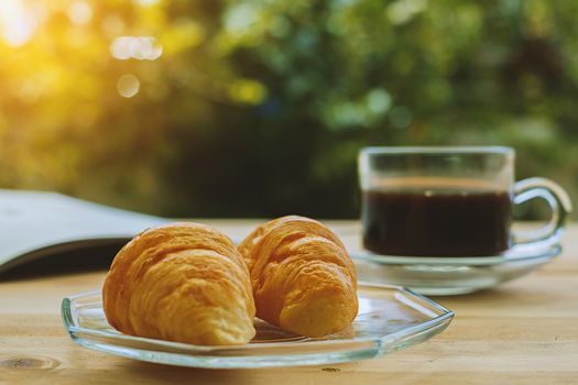 Croissants, a cup of coffee and opened book on blurred green natural background, selective focus and vintage retro color