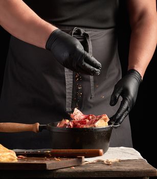 chef in black uniform and latex gloves seasoning raw chicken meat in a black cast-iron frying pan, cooking