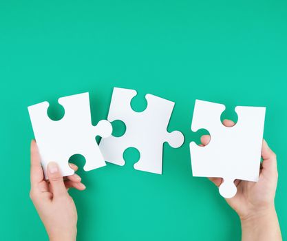 white big puzzles in female hand on green background, business concept, copy space 