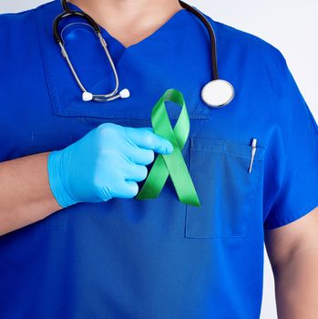 doctor in blue uniform and latex gloves holds a green ribbon as a symbol of early research and disease control, symbol of Lyme disease, kidney transplantation and organ donation