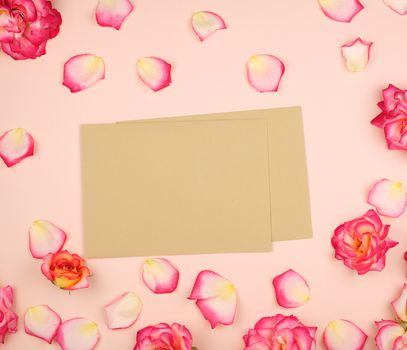 pink rose buds and brown paper envelope on a beige background, top view, flat lay