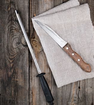 old sharp knife and sharpener with a handle on a gray wooden background, top view