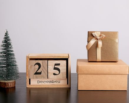 wooden retro calendar from blocks with the date of December 25, Christmas decorative tree and cardboard boxes with gifts, white background
