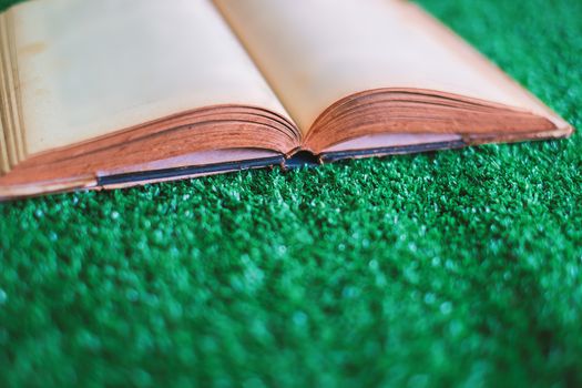 Old opened book on the plastic artificial green grass