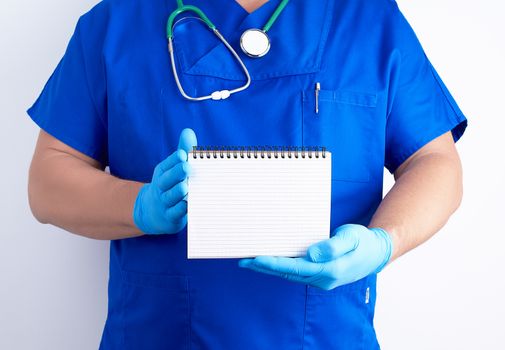 doctor in blue uniform and sterile latex gloves holding open blank notebook, white background, copy space