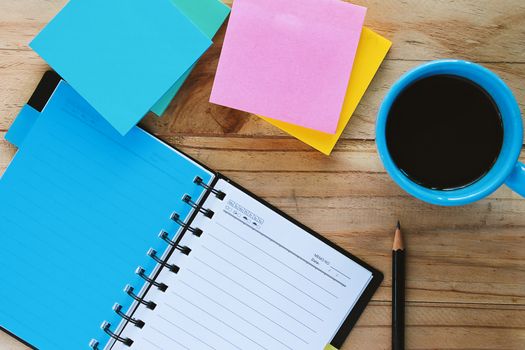 Top view of notebook, a cup of coffee, pencil and note pad on the wooden table, space for thinking and writing with the drinking time